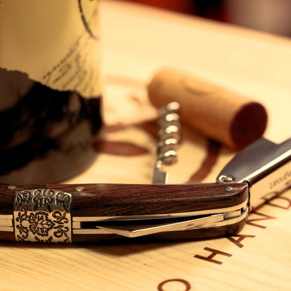 Primitivo Sommelier Corkscrew laying flat on a wooden box beside a bottle of Ares Shiraz
