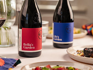 Bottles of Bella's Garden and Lily's Garden on a tablecloth surrounded by plates of food and decor.