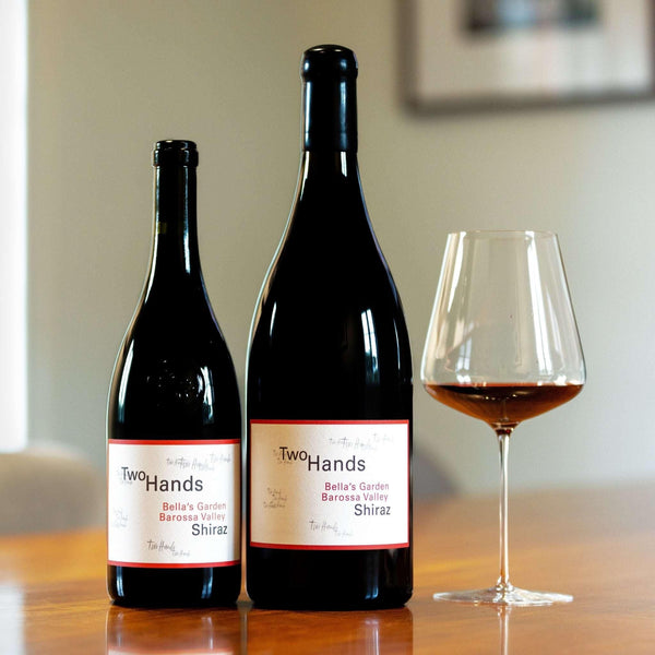 Bottle of Bella's Garden Shiraz 750mL and 1500mL magnum with a glass poured on a wooden table.