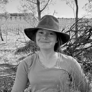 Lara part of our vineyard team wearing a wide-brimmed hat in a natural setting with trees and open space.